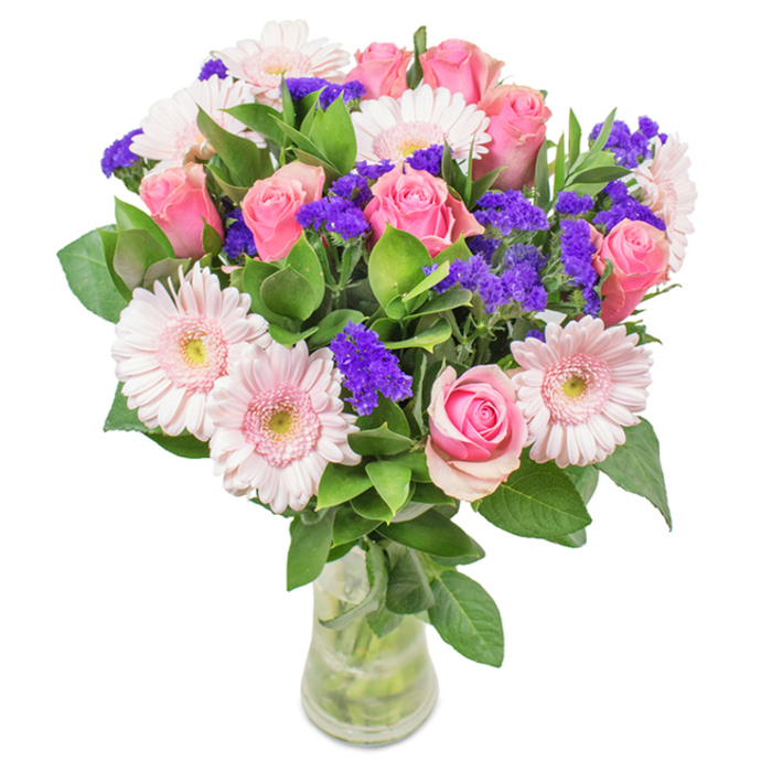 A vibrant display of floristry from Feltham Flowers, this arrangement features an elegant combination of approximately 7-9 medium pink roses nestled among 5-7 pale pink gerbera daisies, all presented in a clear glass vase against a bright, inviting background. The roses, some still tightly furled and others spiraling open in stages, exude classic beauty and tenderness-a fitting touch for celebratory occasions or to brighten a space along Hanworth Road. The gerberas offer a sunny counterpoint, their large, circular heads with light, near-white centers bringing a sense of lightness and charm, as if caught in a spring breeze over Feltham Park. Intermingled throughout are clusters of intense, jewel-toned purple statice, lending texture and drama while instilling a feeling of cheerful exuberance. Fresh, deep green foliage underpins the entire bouquet, ensuring each bloom is highlighted and that the whole feels full of life and vitality. Stems and cool water glint through the glass, testifying to the freshness and careful handling of every flower. Whether delivered for a birthday, marking a milestone, or simply adding a touch of joy to a home or office in Feltham, this bouquet radiates care, beauty, and the heartfelt craftsmanship of the local Feltham community.